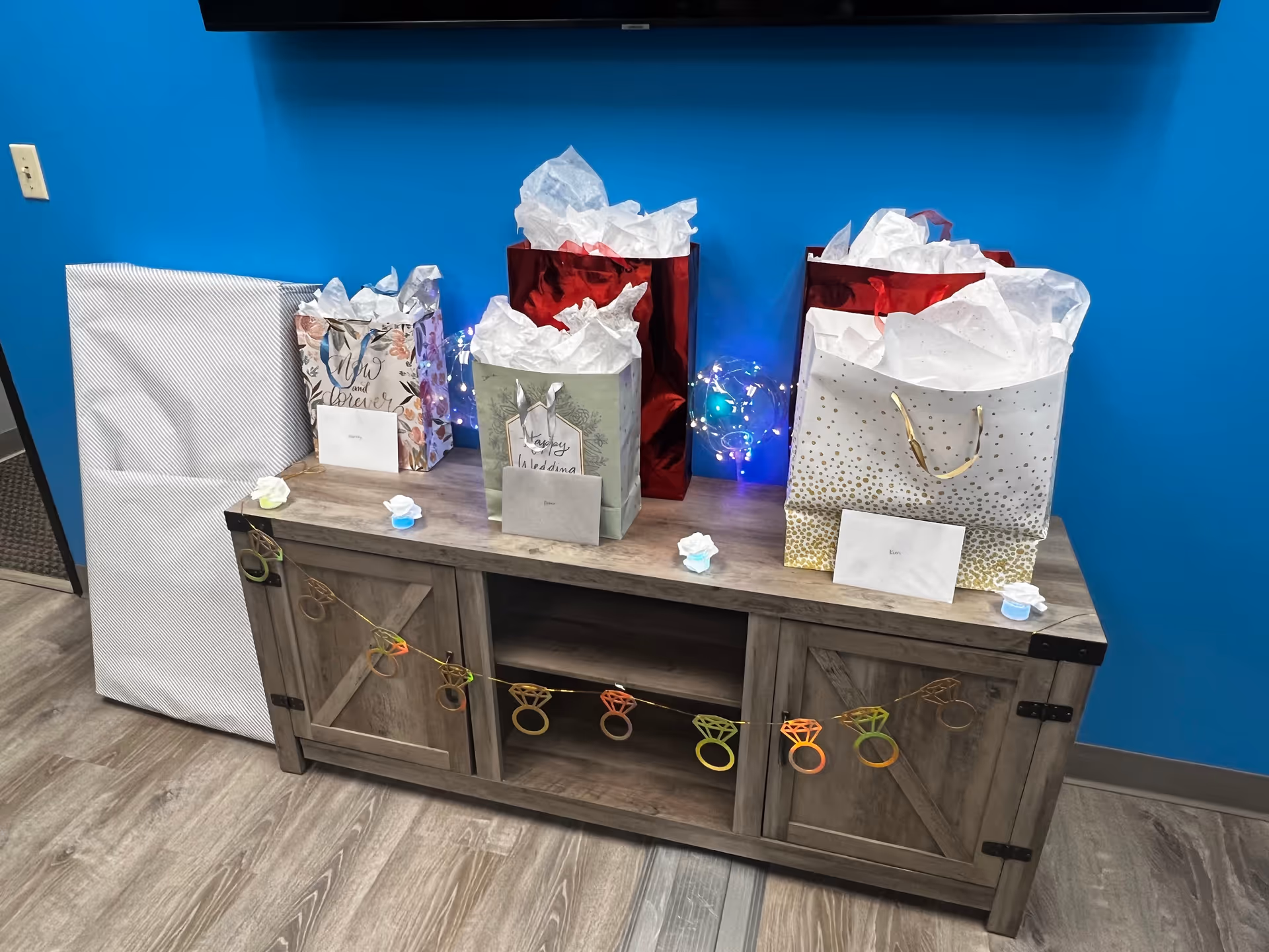 Gift bags with tissue paper sit on a wooden cabinet against a bright blue wall.