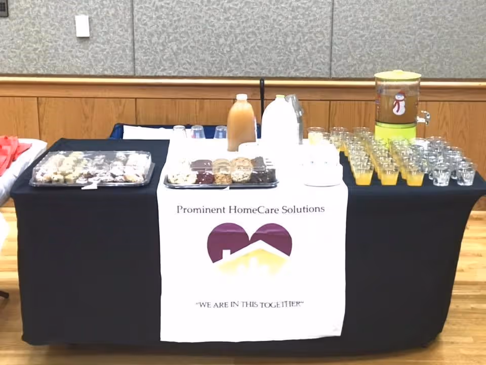 Indoor refreshment table with a Prominent HomeCare Solutions banner, pastries, and drinks.