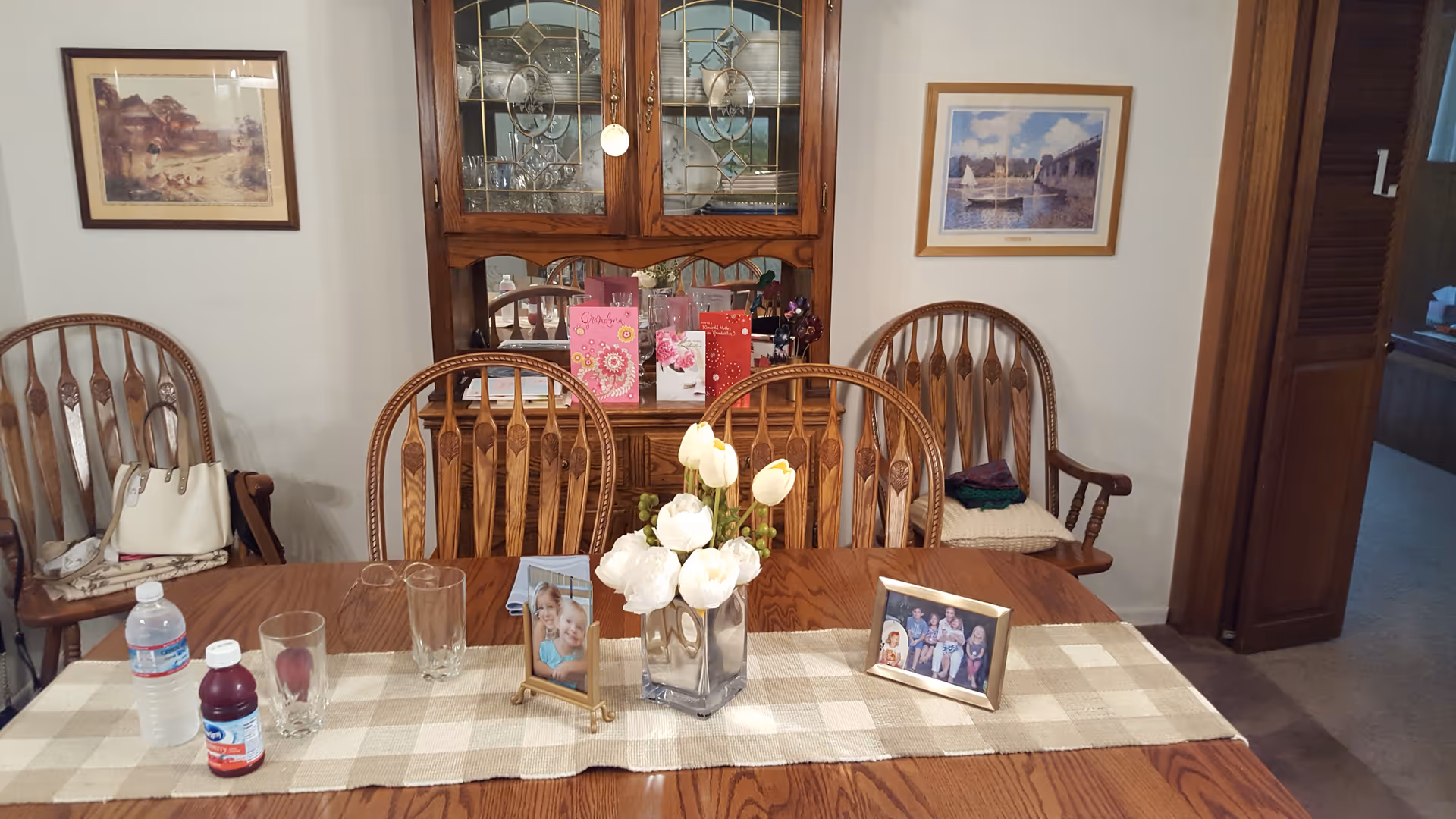 Wood dining table with chairs, photos, and a china cabinet in a warm dining room.