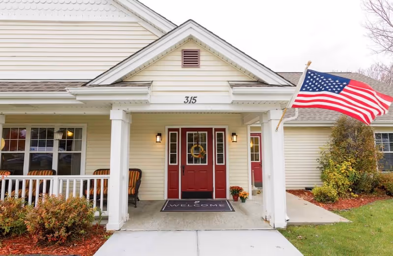 Front entrance of West Ridge Hills & Estates with a porch, red doors, and American flag.