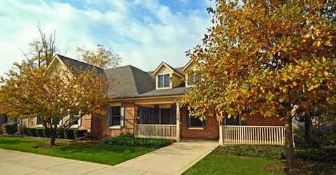 Brick facility building with a front porch, trees, and a sidewalk.