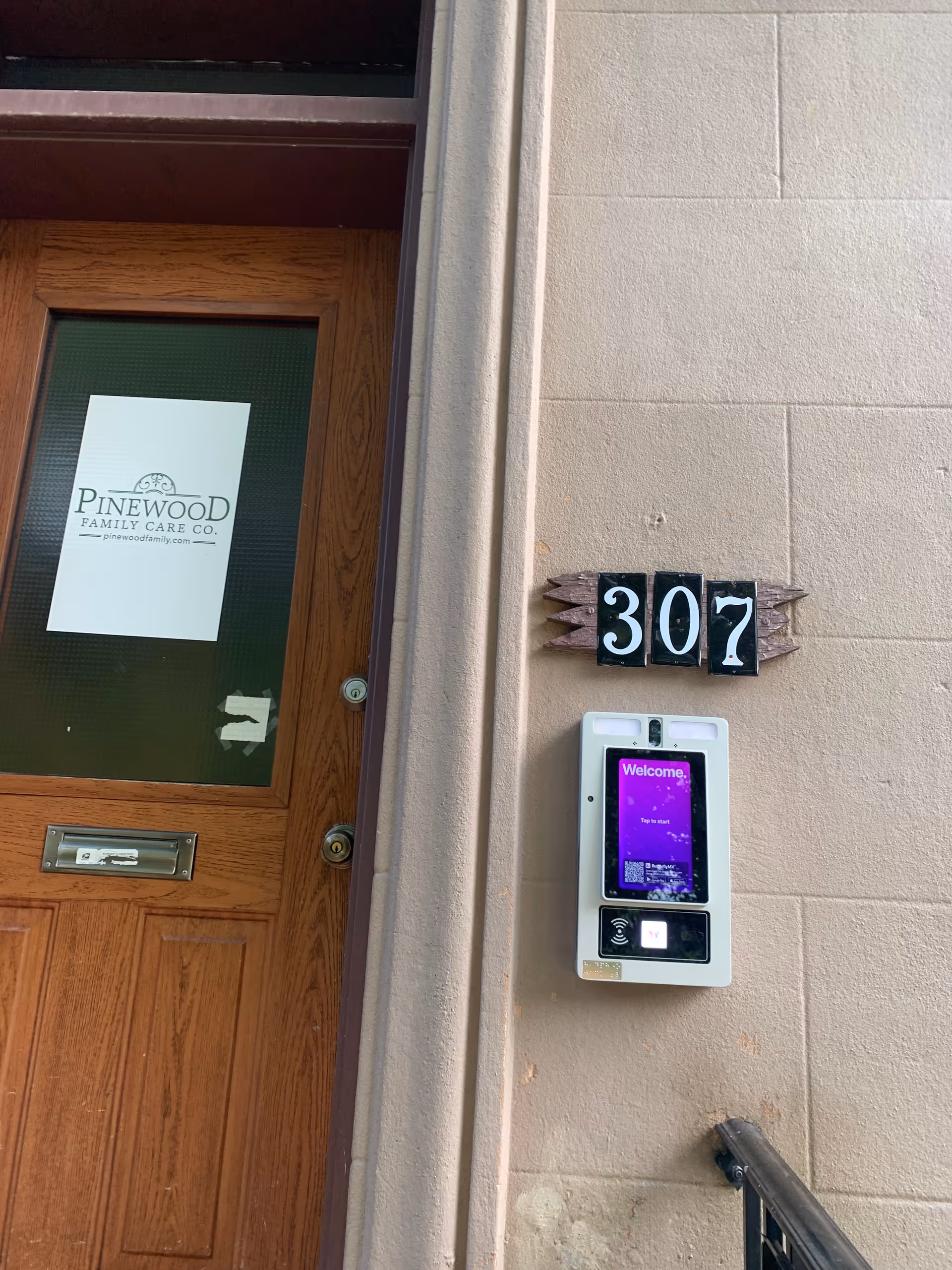 Wooden front door with Pinewood Family Care sign, building exterior and 307 plaque with access panel.