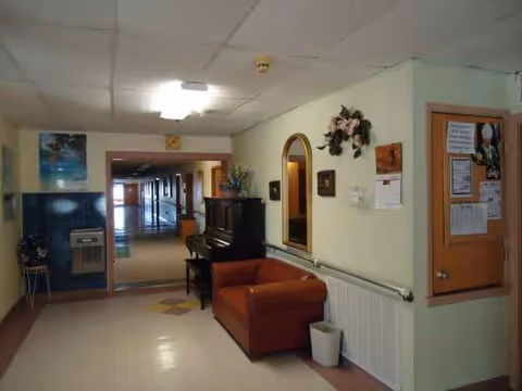 Corridor scene in John Paul II Nursing Home with seating, piano, mirrors, and bulletin board.