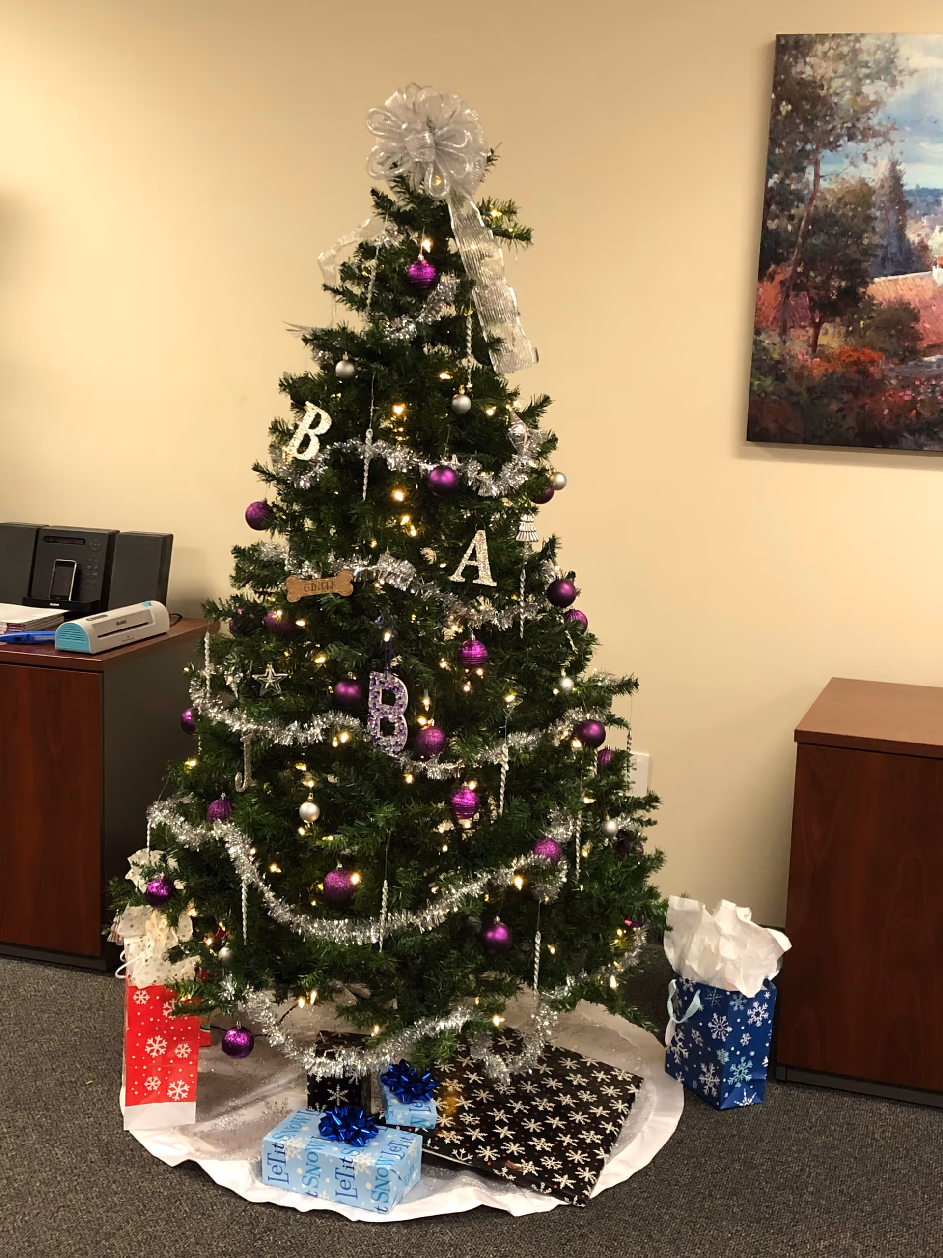 Indoor Christmas tree with purple ornaments and wrapped gifts in a senior living facility.