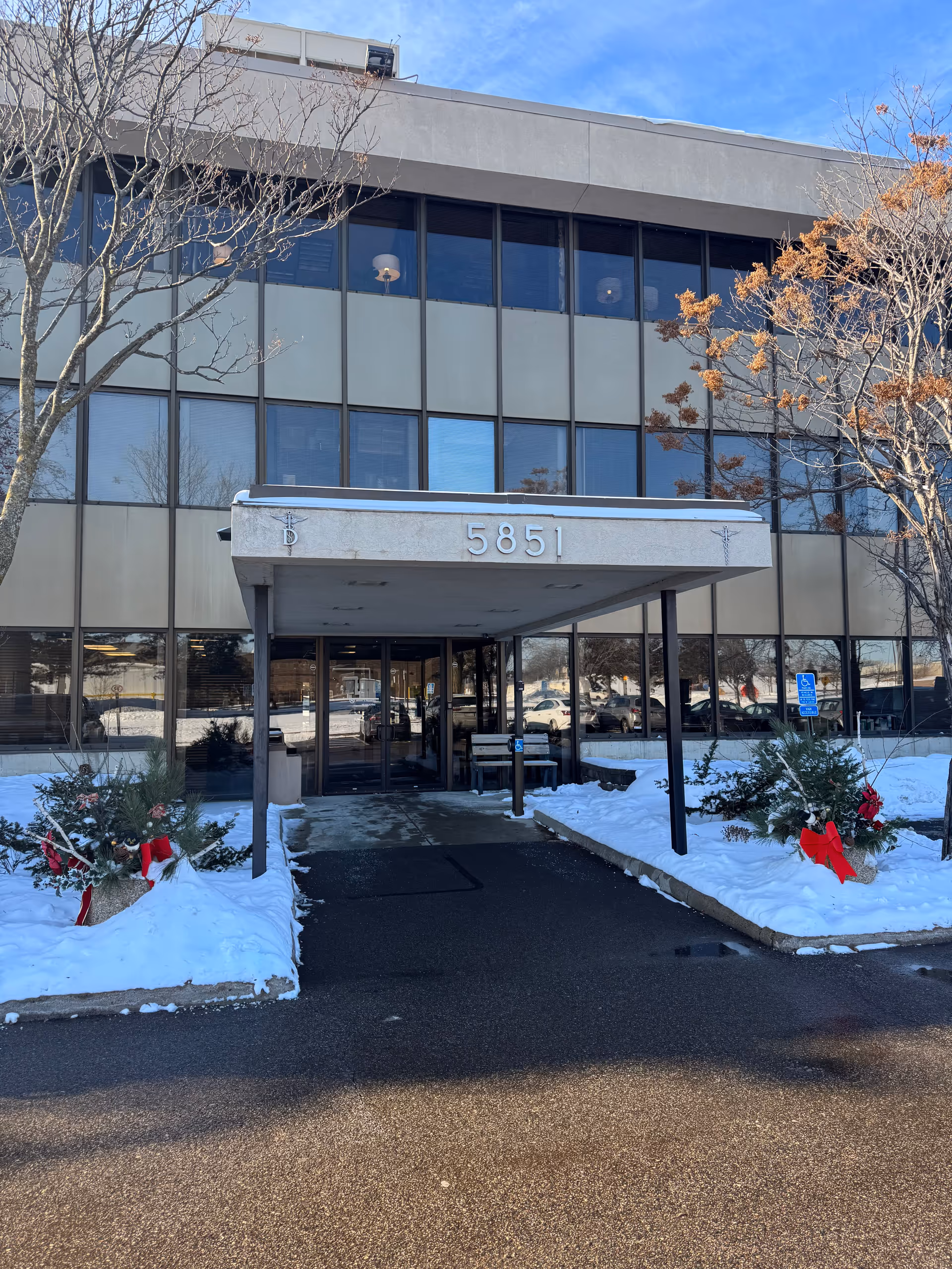 Front entrance of a glass-front building with a covered canopy and snowy landscaping.