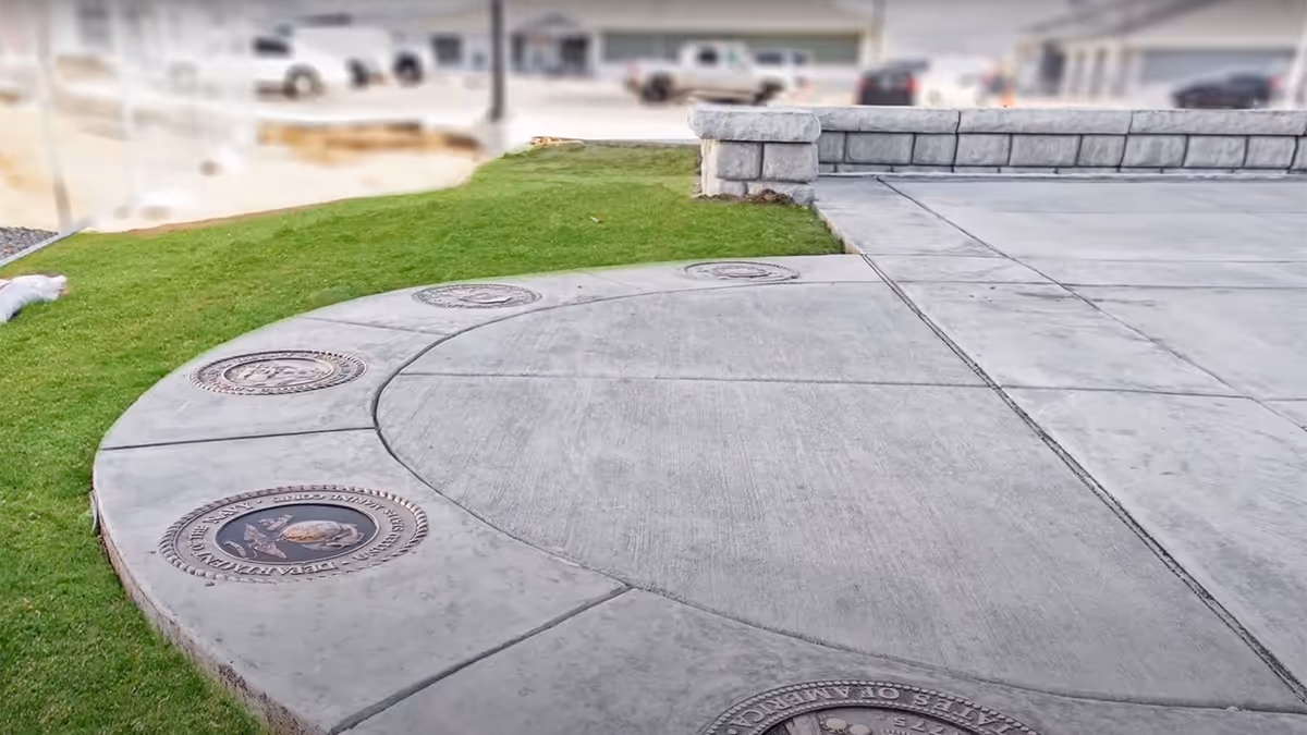 Circular concrete plaza with bronze medallions beside a grassy area at a veterans home