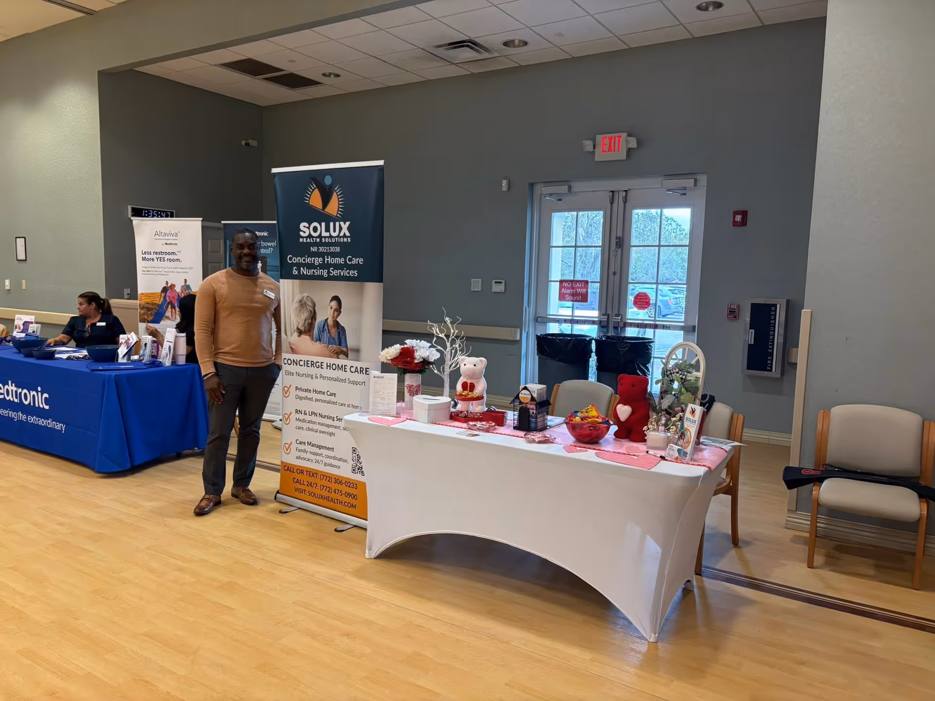 A man stands beside a SOLUX Health Solutions banner at an indoor expo booth.