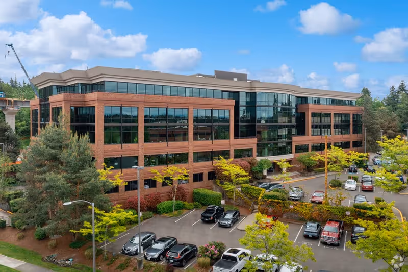 Three-story brick senior living building with large glass windows and a parking lot.