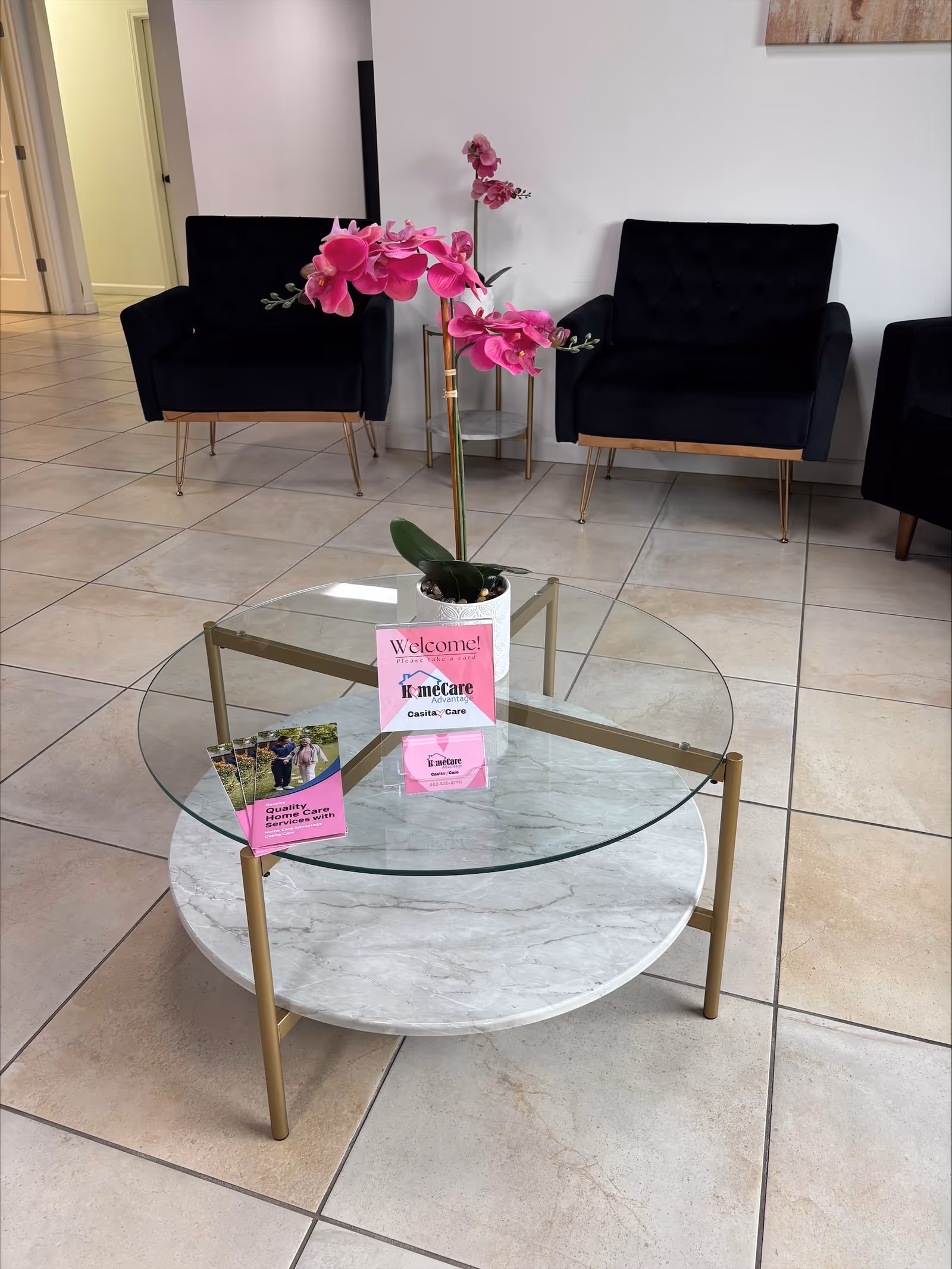 Lobby seating area with glass coffee table, pink orchid, and welcome brochures.