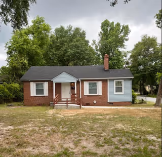 Front view of a small brick-and-blue single-story house with a porch.