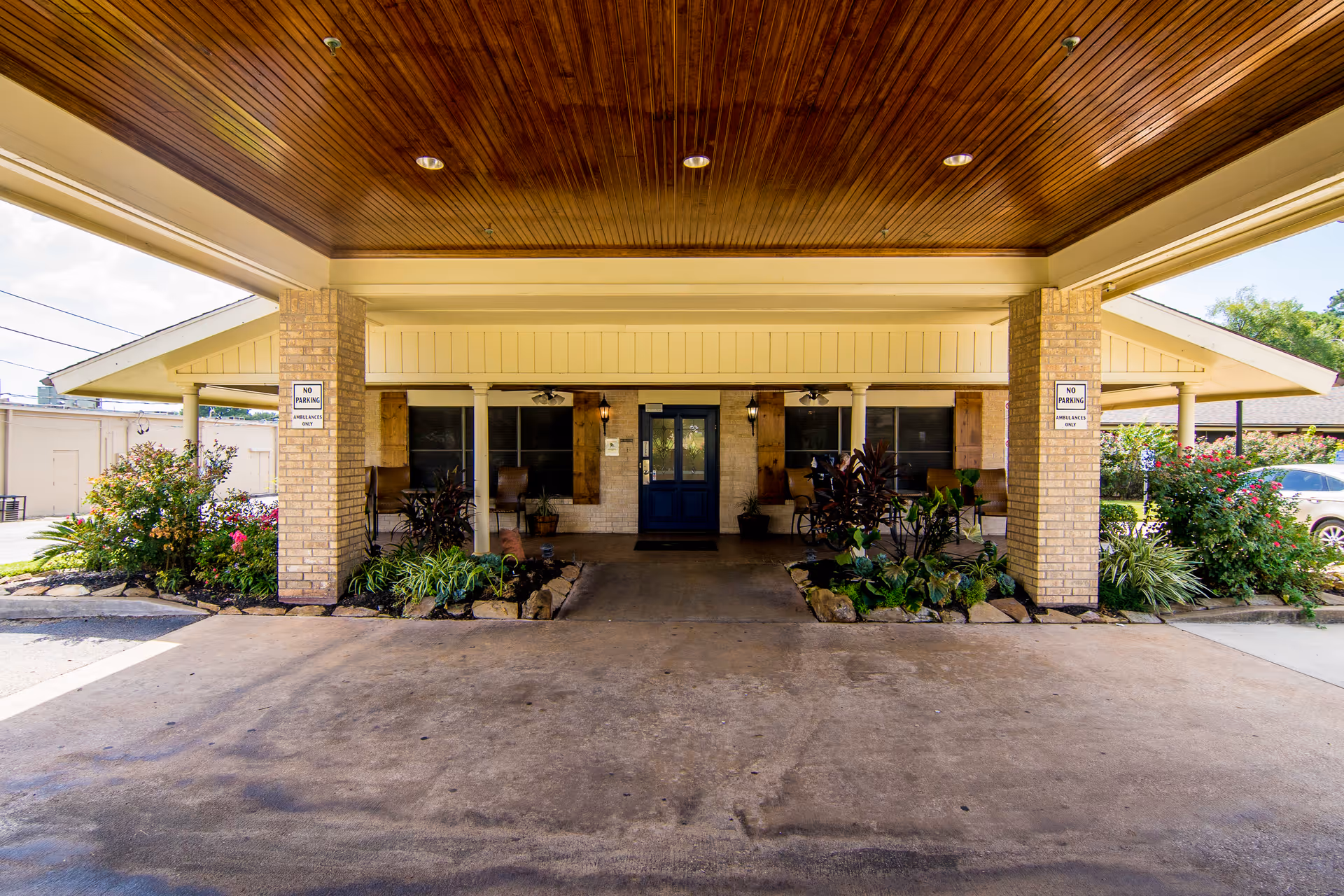 Covered porte-cochère entrance of Conroe Health Care Center with brick columns, landscaping, and a central double door.