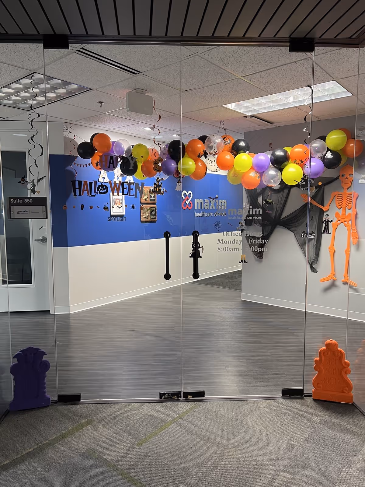 Glass double doors open to a decorated hallway with Halloween balloons at Maxim Healthcare Virginia Beach.