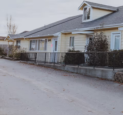 Exterior view of a single-story assisted living building with a railing and shrubs.