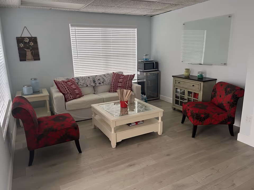 Cozy living room with a white sofa, two red-patterned chairs, and a glass coffee table.