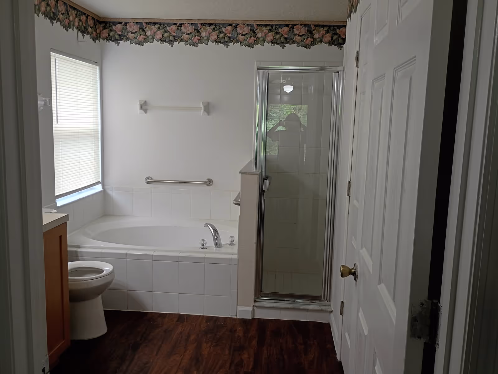 Bathroom with tub, separate shower, toilet, vanity, and floral border wallpaper.