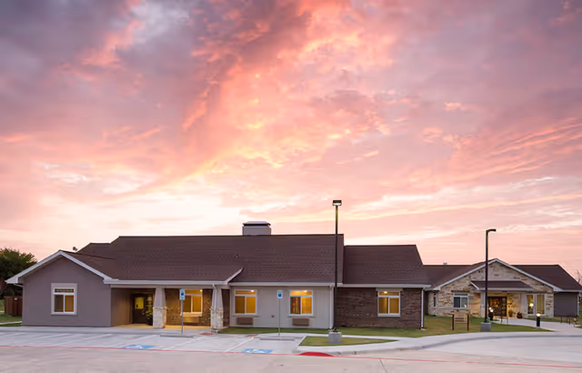 Exterior view of Oxford Glen at Owasso, a single-story senior living building at sunset.