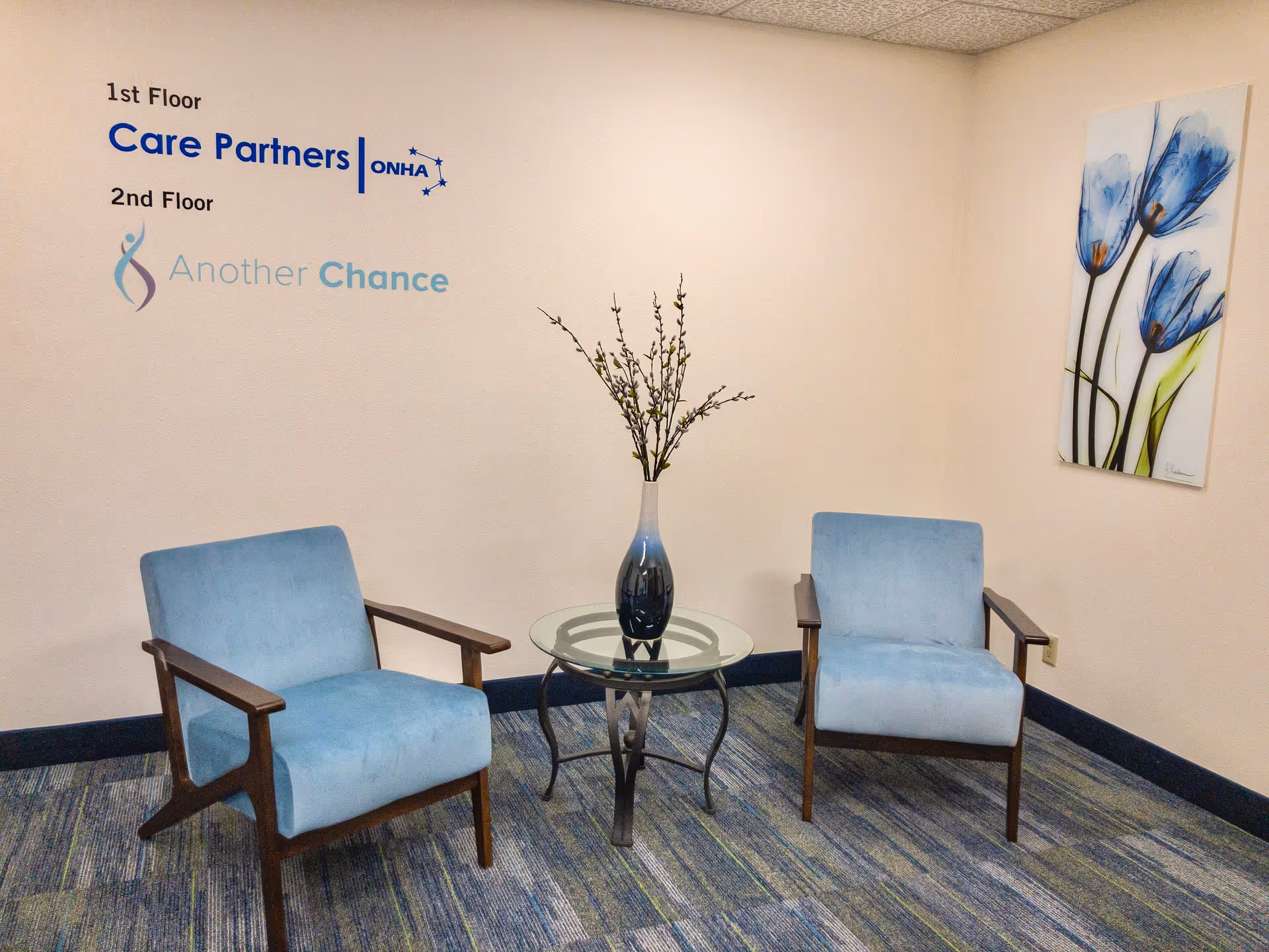 Two blue chairs flank a glass table in a small interior waiting area.