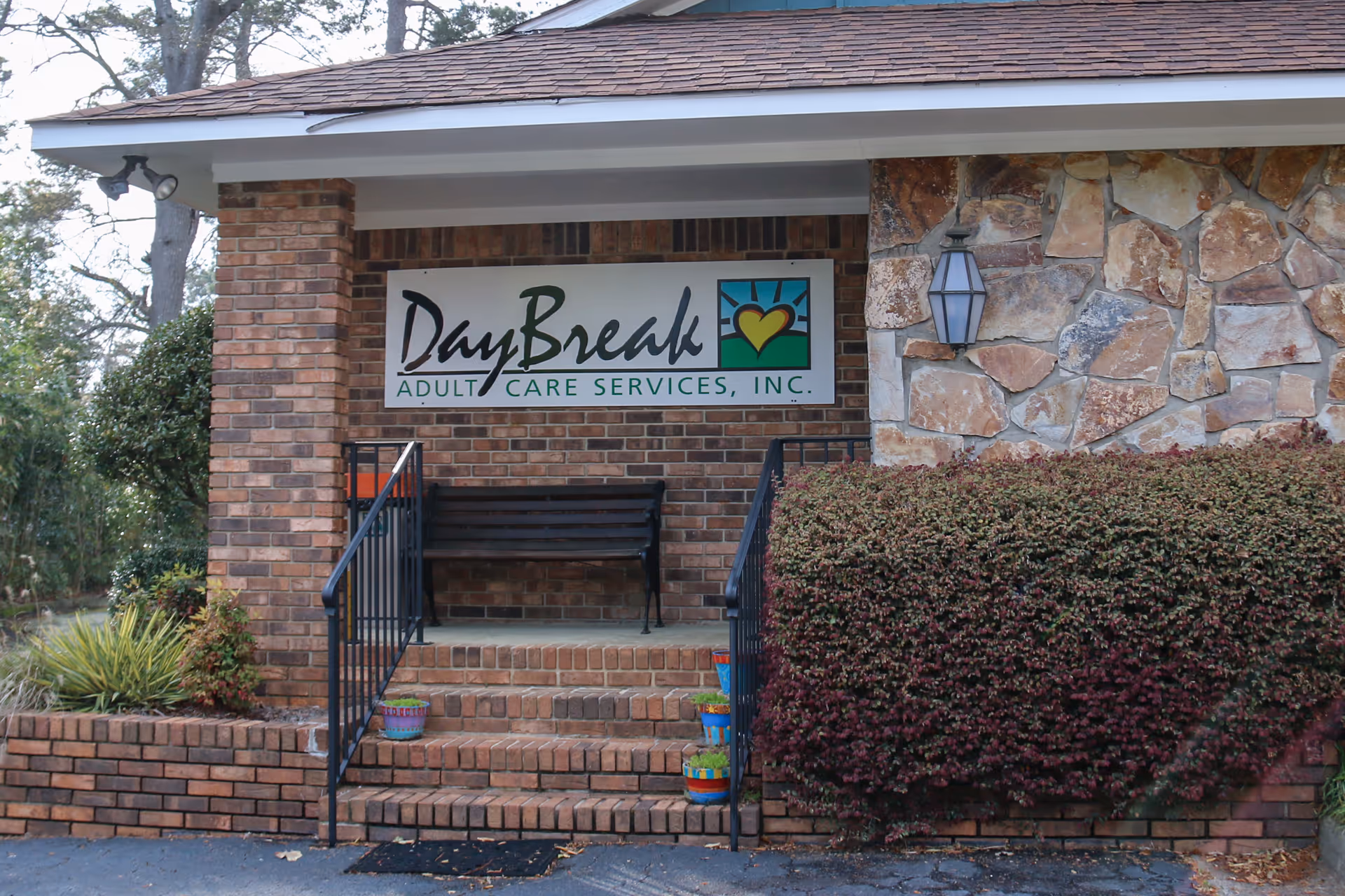 Brick and stone building entrance with DayBreak Adult Care Services sign and bench.