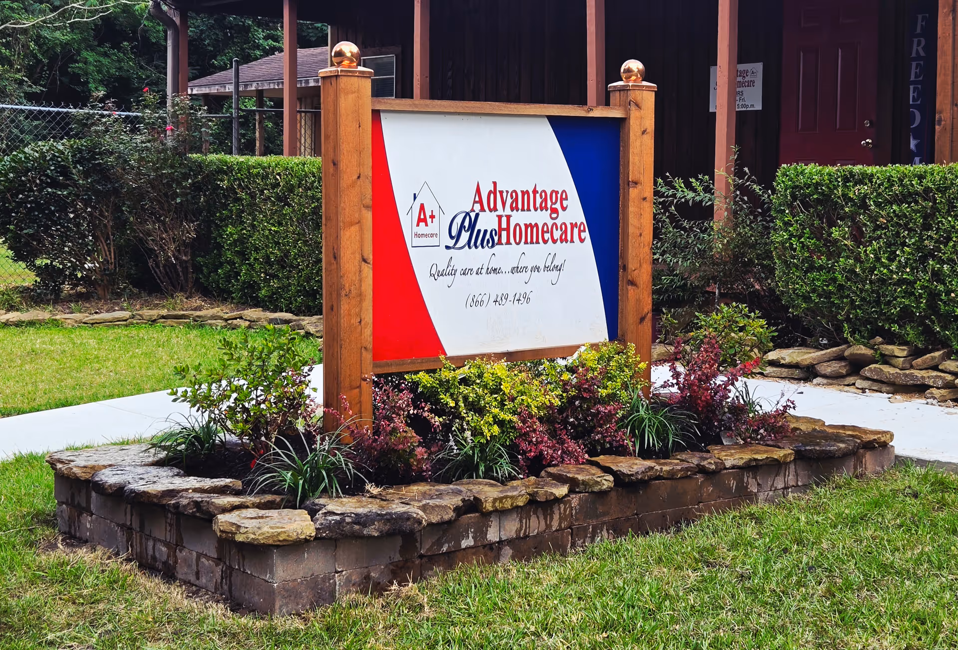 A wooden-framed sign for Advantage Plus Homecare sits in a landscaped front yard.