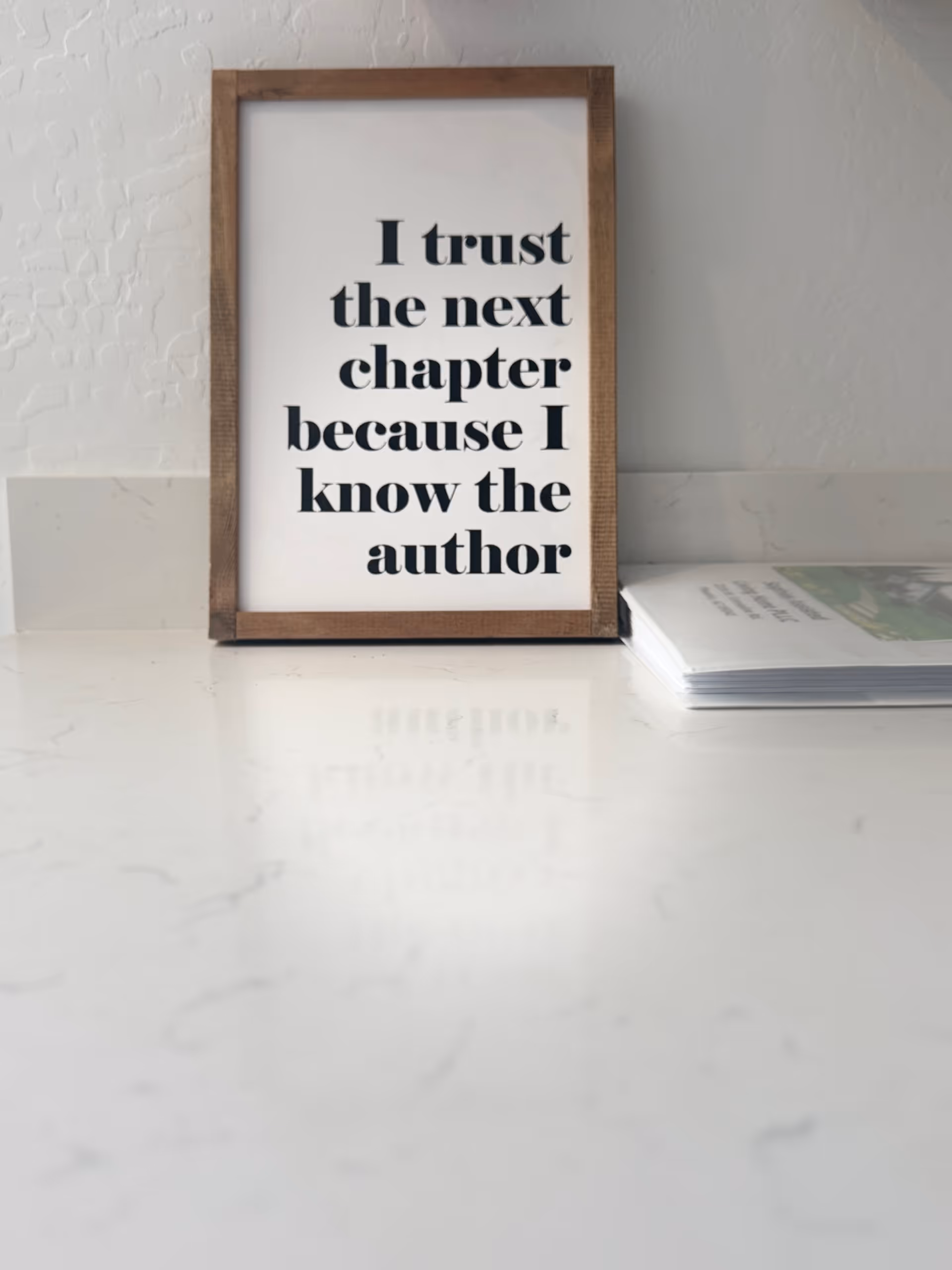 Framed quote on a white countertop beside a small stack of papers