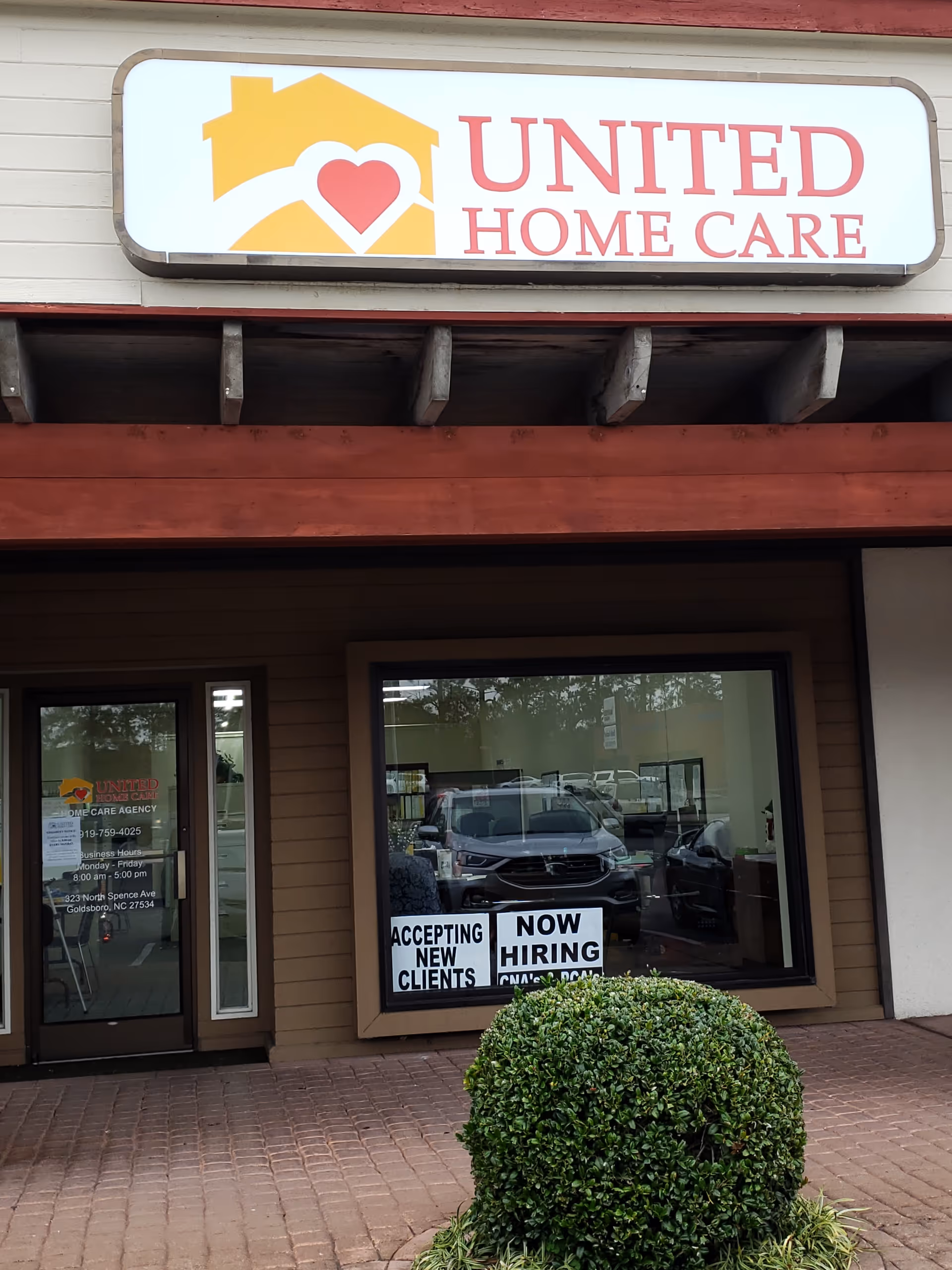 Exterior of United Home Care storefront with sign, windows, doorway, and a shrub.