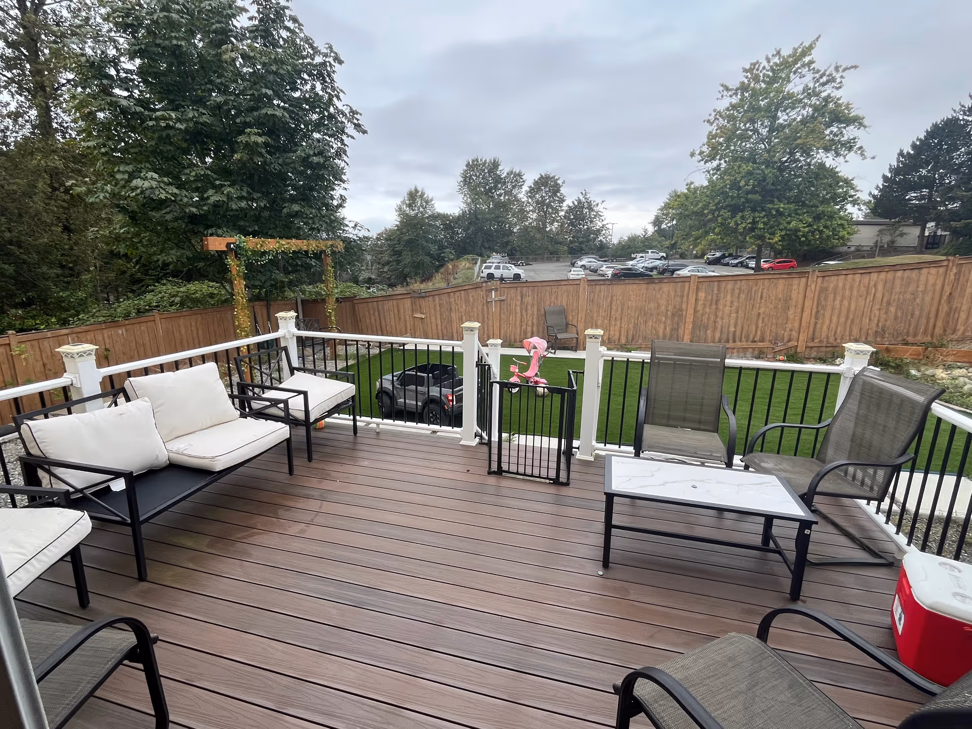 Outdoor wooden deck with seating and a fence, overlooking a parking lot.