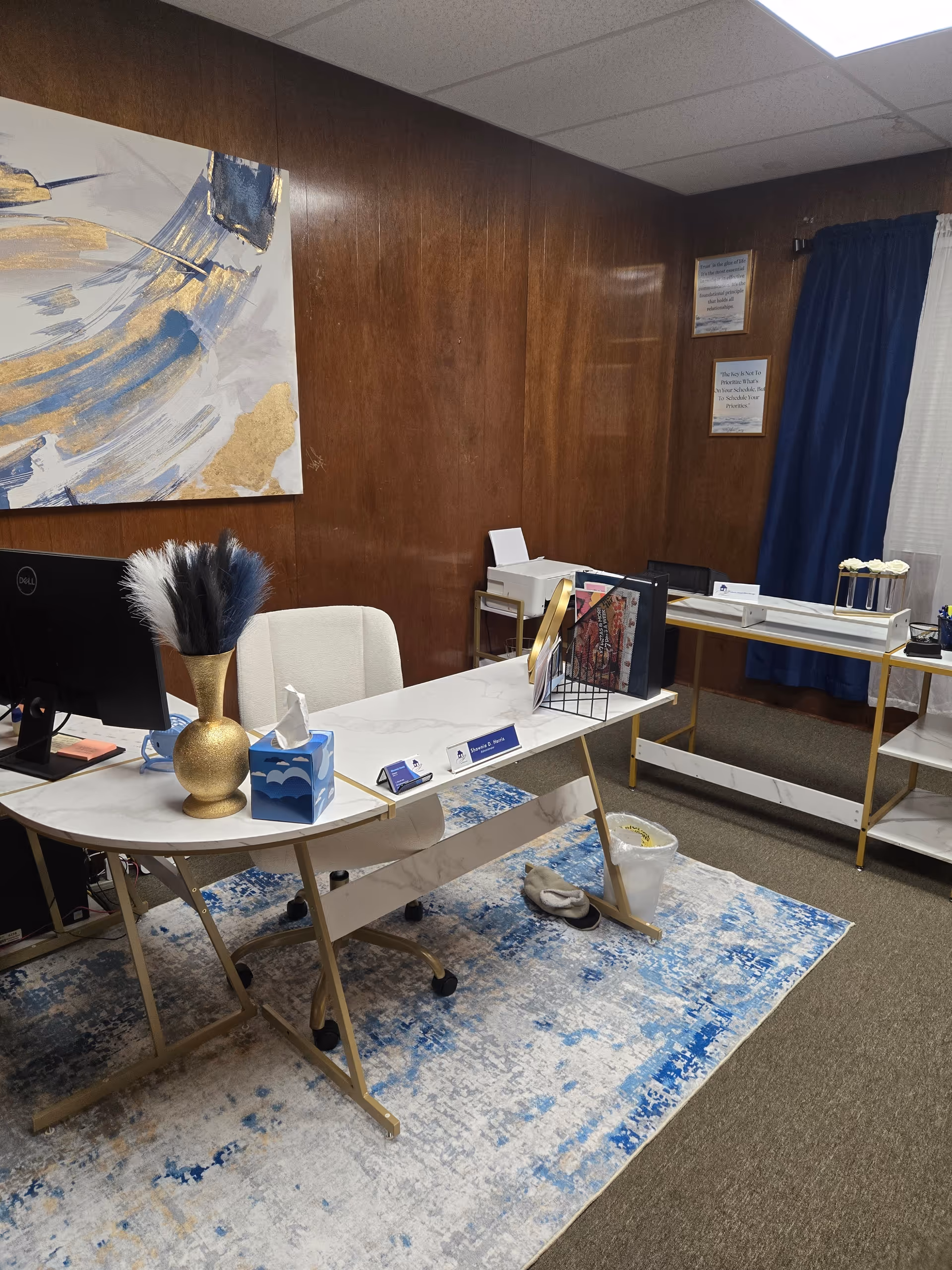 Administrative desk in a wood-paneled office area with blue rug and abstract wall art.