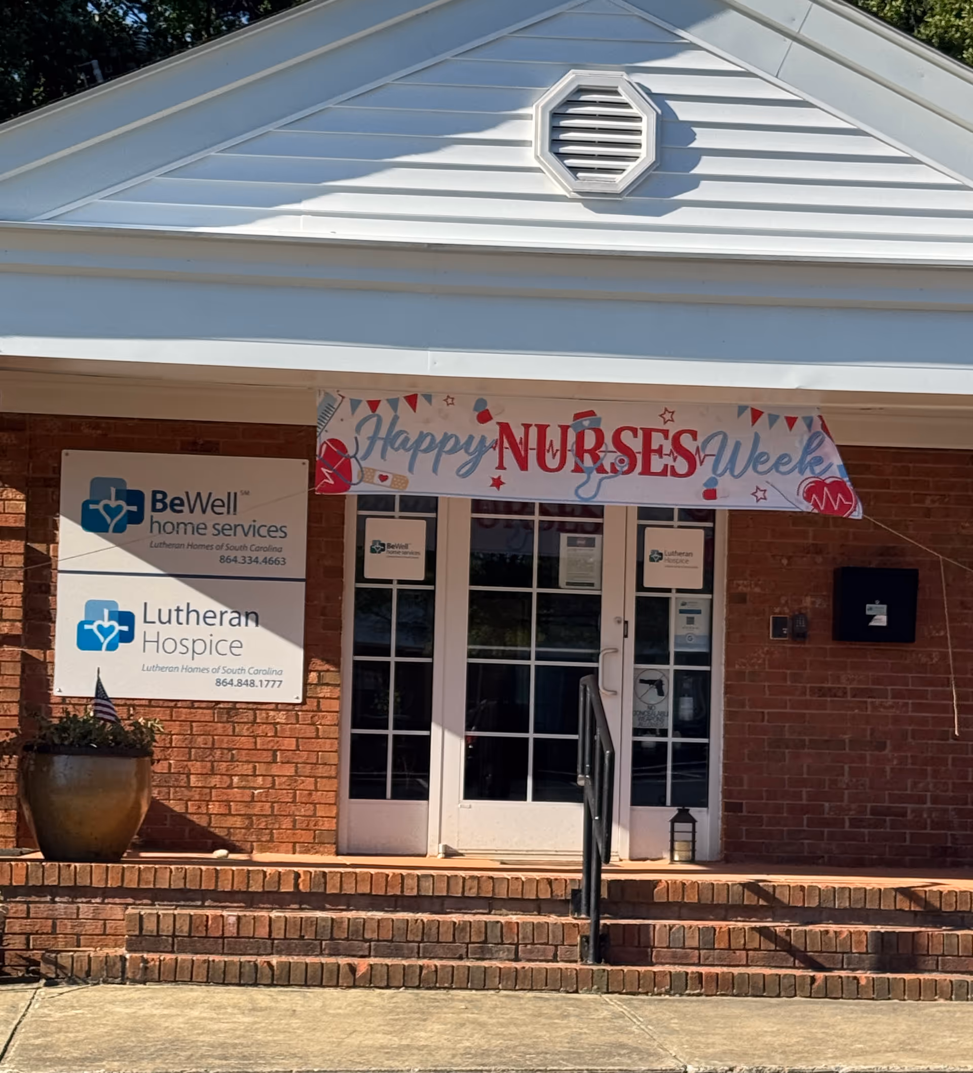 Brick building entrance with a 'Happy Nurses Week' banner and BeWell Hospice signs.