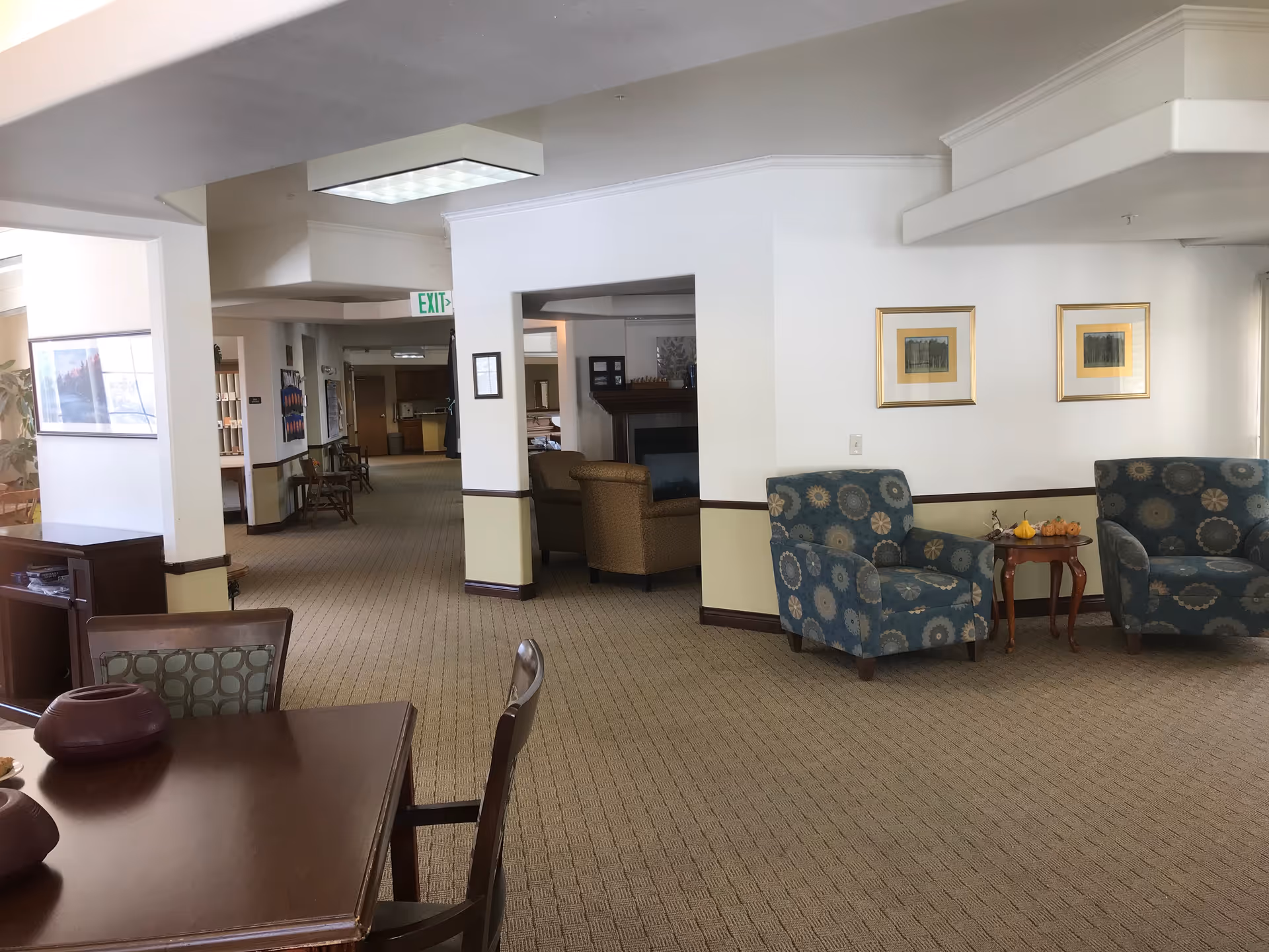 Bright senior living lounge with blue patterned chairs, a small table, and wall art.