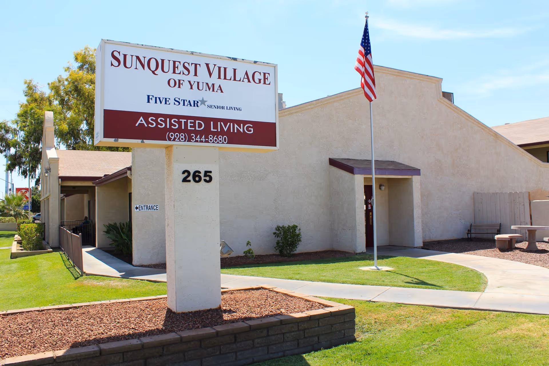 Exterior view of SunQuest Village of Yuma with sign and flag.