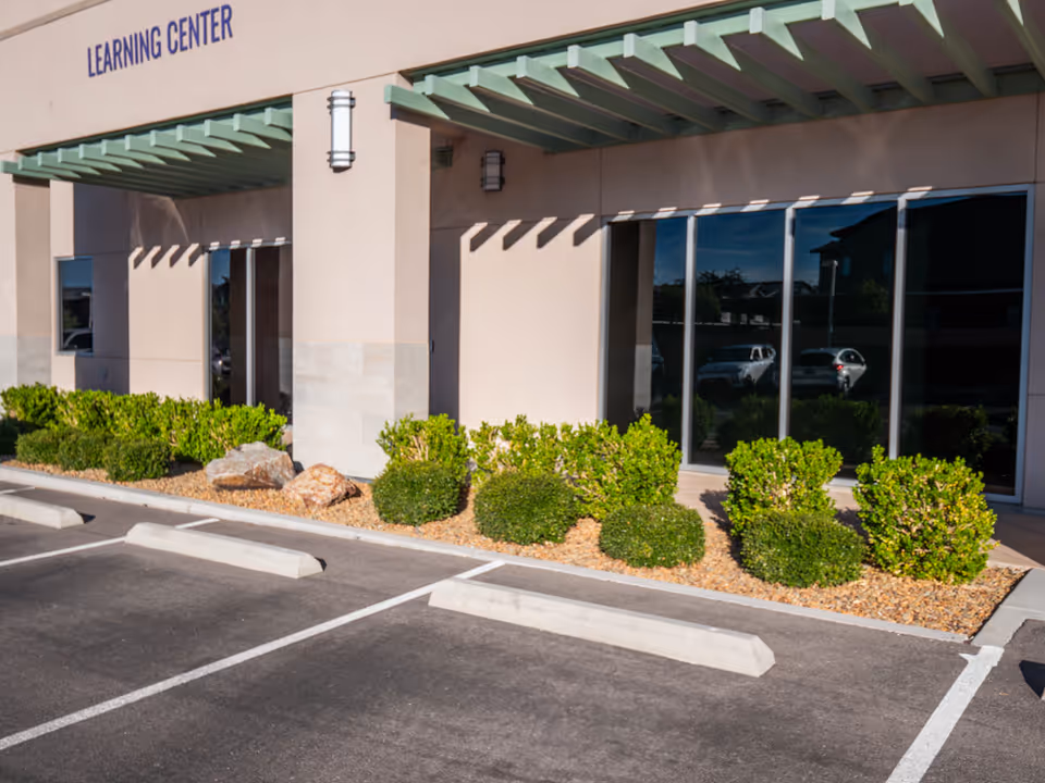 Exterior of a facility with Learning Center sign, glass windows, and landscaped parking area.