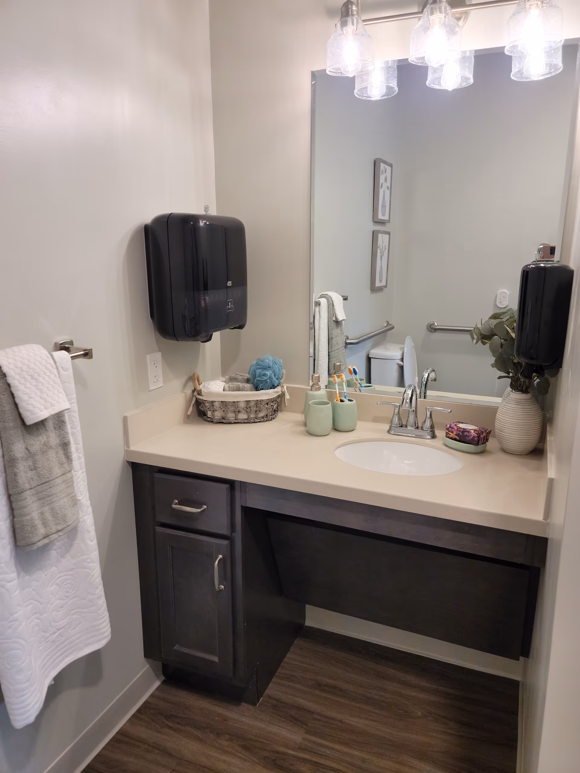 Small bathroom with sink, mirror, towel, and countertop accessories in a senior living facility.