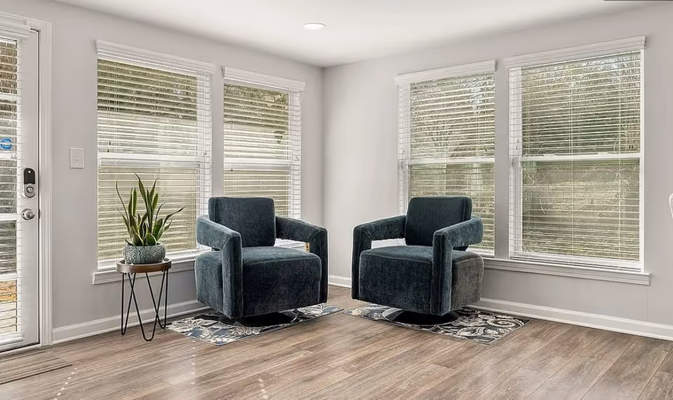 A bright senior living lobby with two teal chairs, a plant, and large windows.