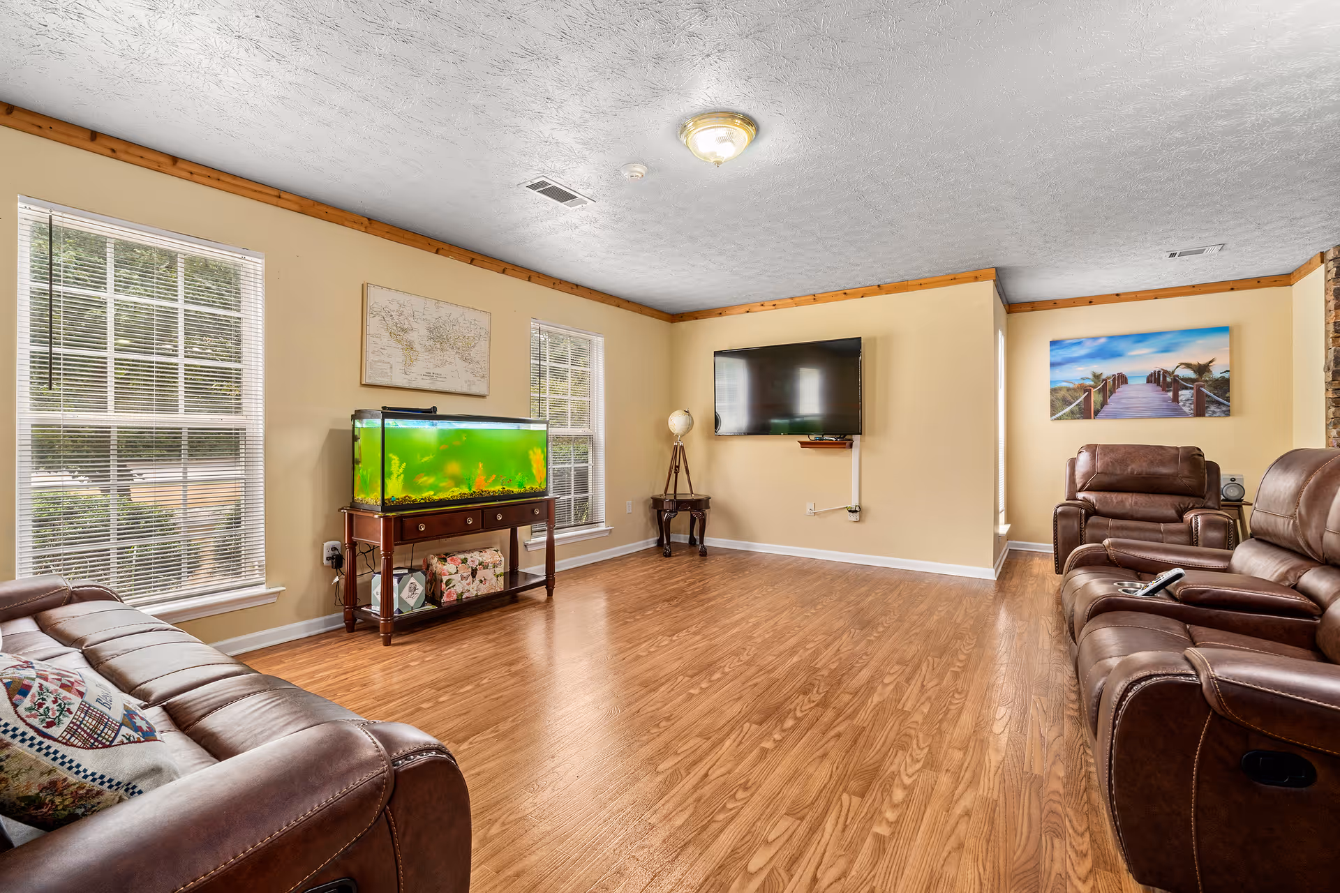 A spacious living room with leather seating, an aquarium, and a wall TV.