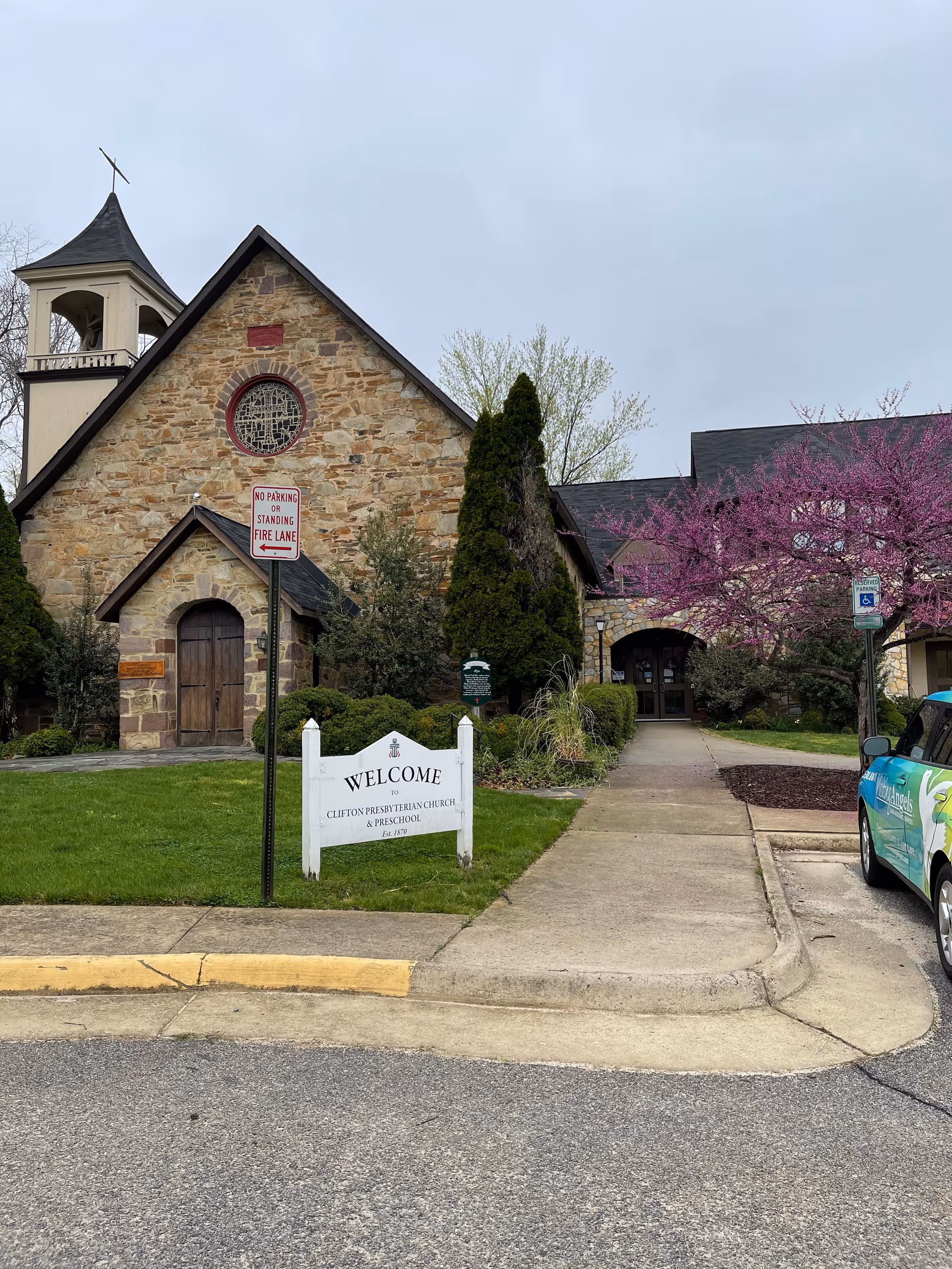 Stone church-style building with bell tower, walkway, and a welcome sign at the front.