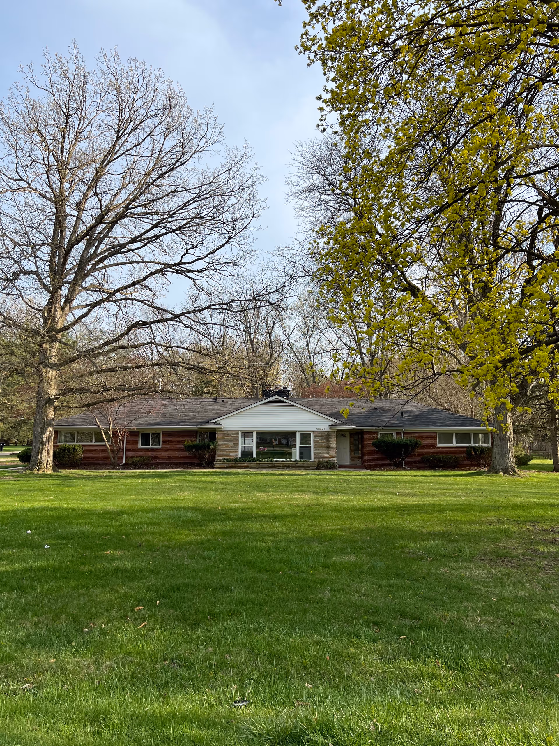 Single-story brick senior living building with a wide grassy lawn and tall trees.