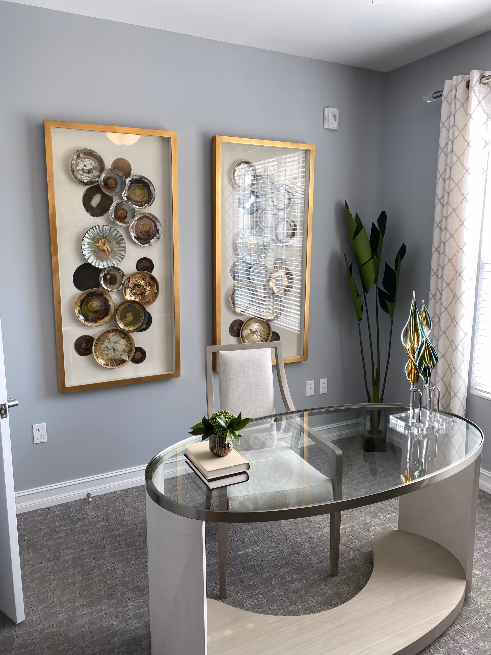 Modern interior with glass desk, two framed circular plate artworks, and a tall plant.