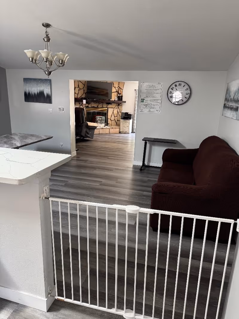 Interior living area with a white gate, couch, chandelier, and doorway to a stone fireplace room.