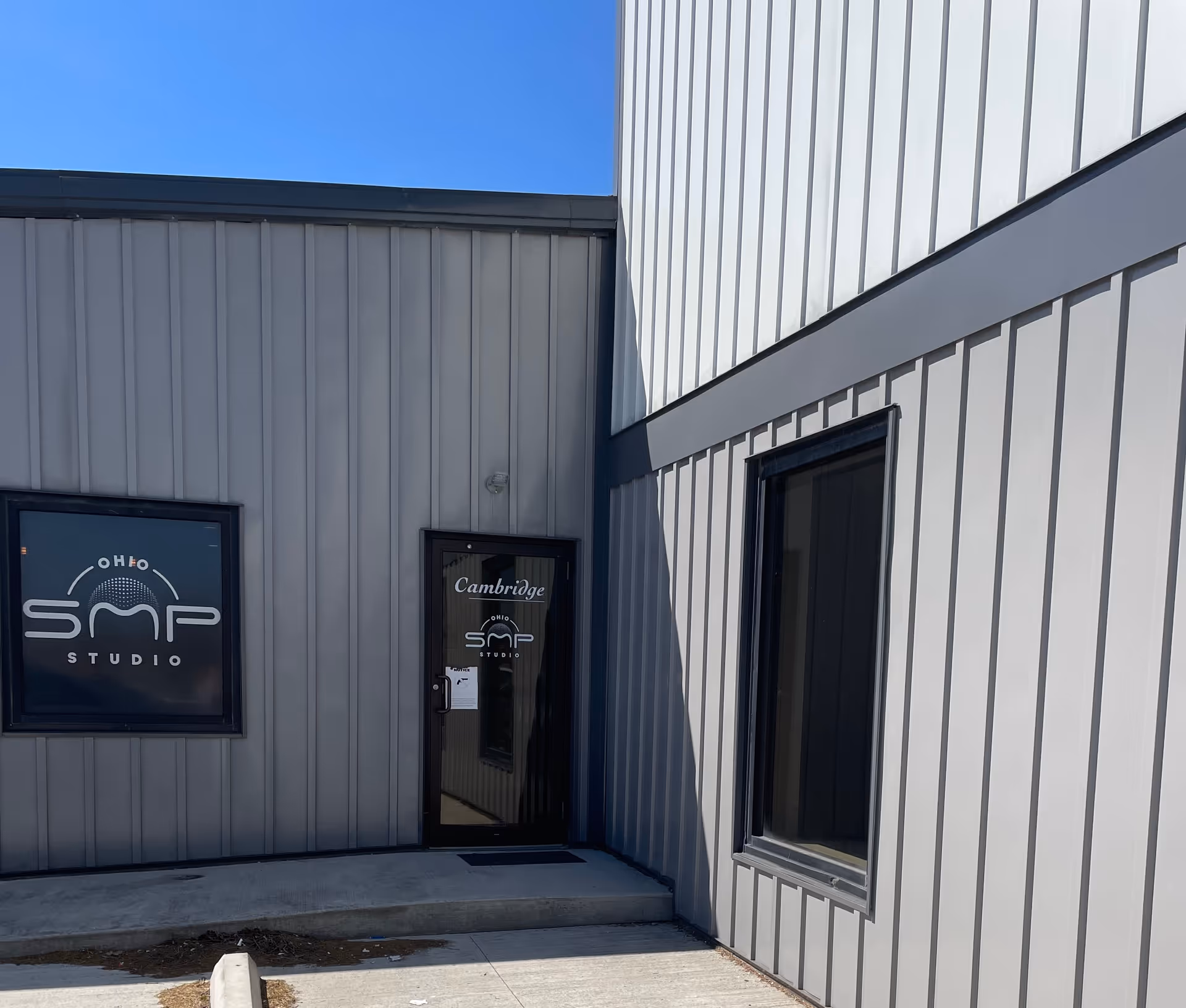 Modern gray metal building exterior with Cambridge sign and glass door entrance.