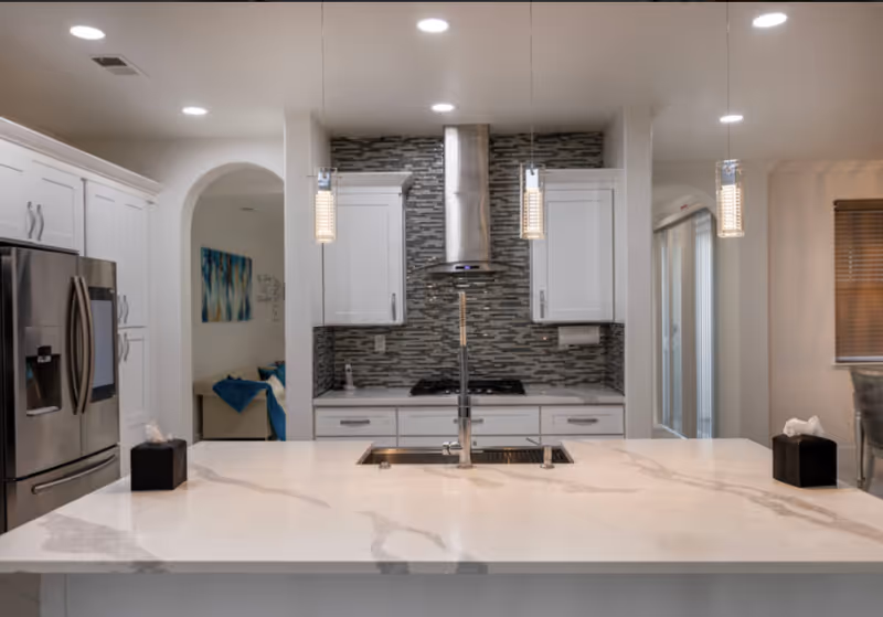 Bright modern kitchen with white cabinets, island, and stainless steel appliances.