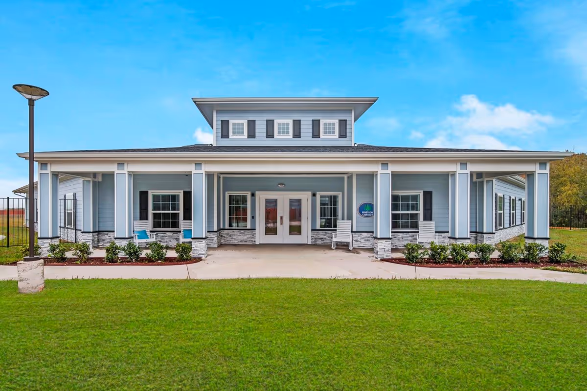 Blue senior living facility with entrance, columns, and manicured lawn under blue sky.