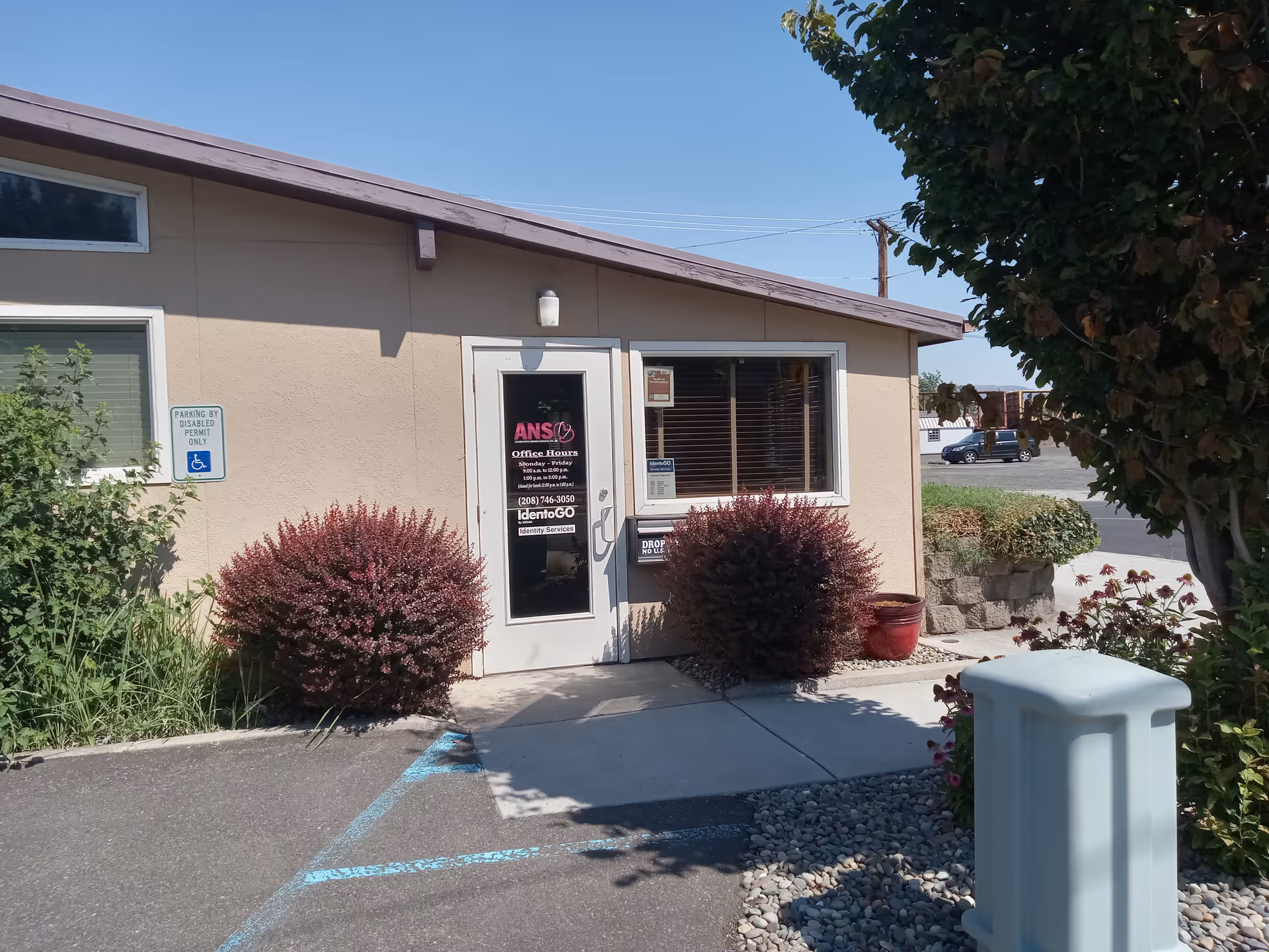 Front exterior of a beige office building with glass door and landscaping.