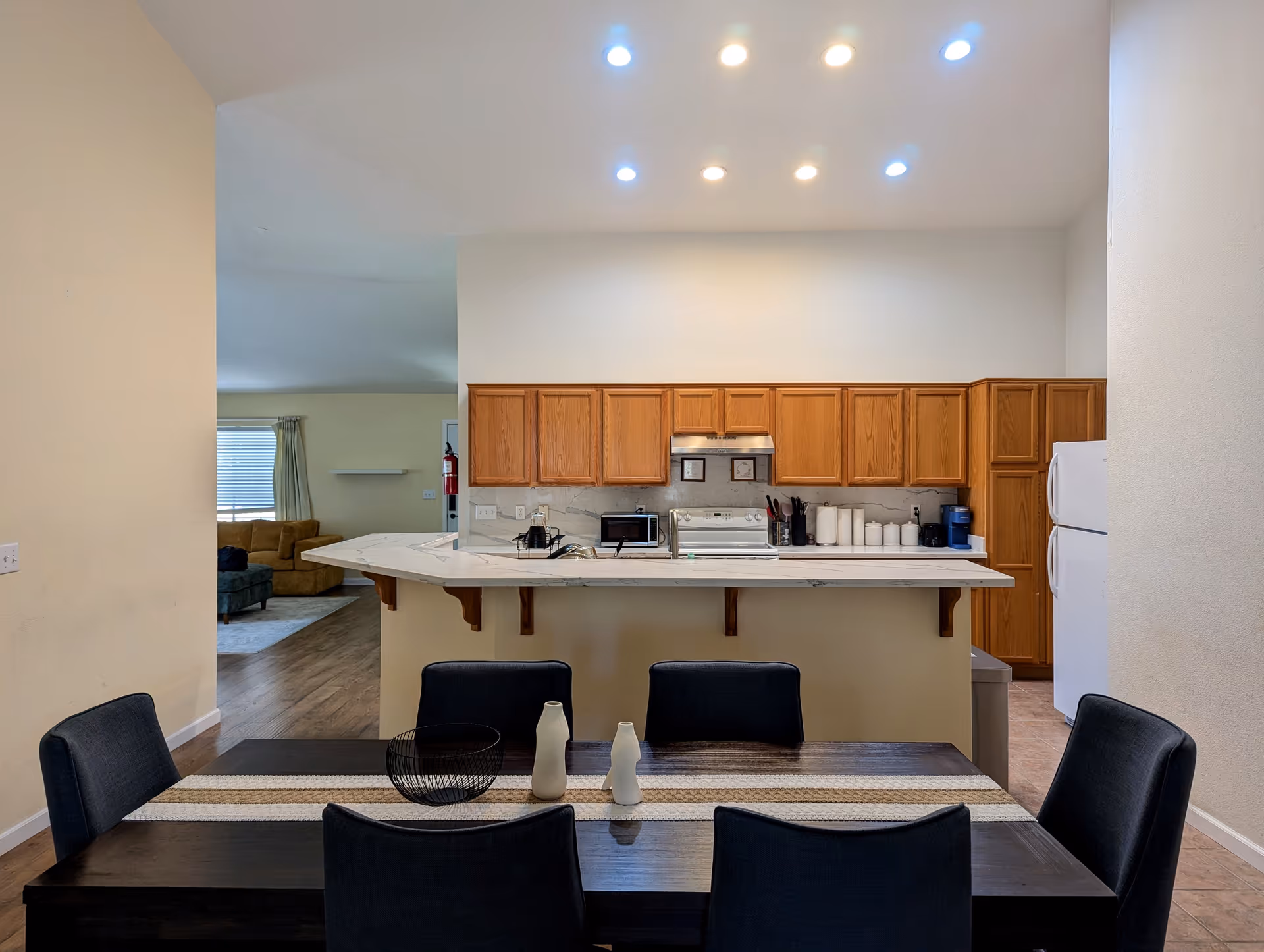 Open-concept kitchen with breakfast bar, wooden cabinets, and a dining table in a senior living facility.