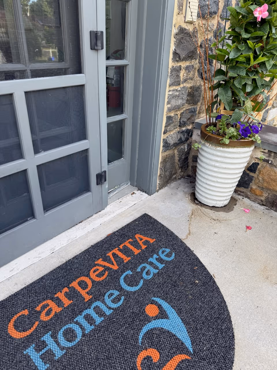 Exterior entrance of CarpeVITA Home Care with a stone wall, potted plant, and mat.