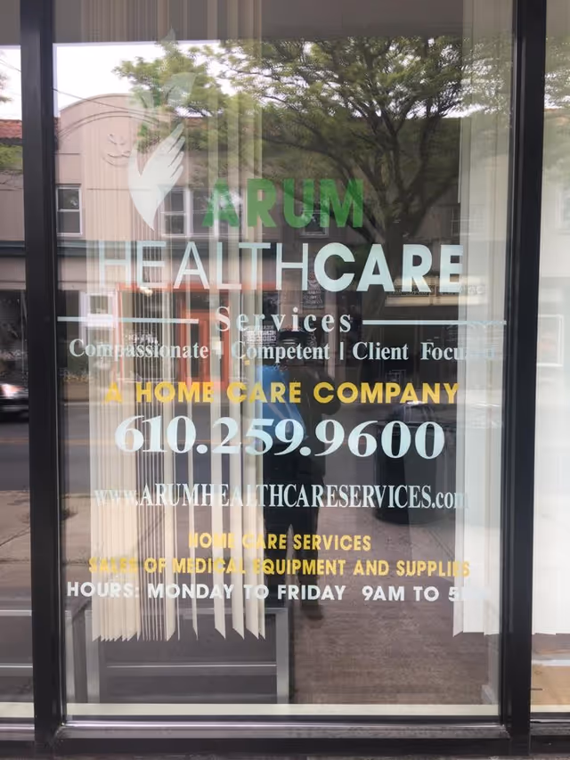 Glass storefront door with Arum Healthcare Services signage and tree reflections