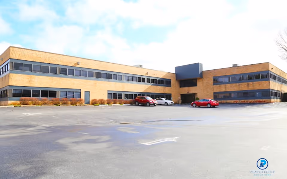 Two-story brick building with expansive windows and a large parking lot in front.