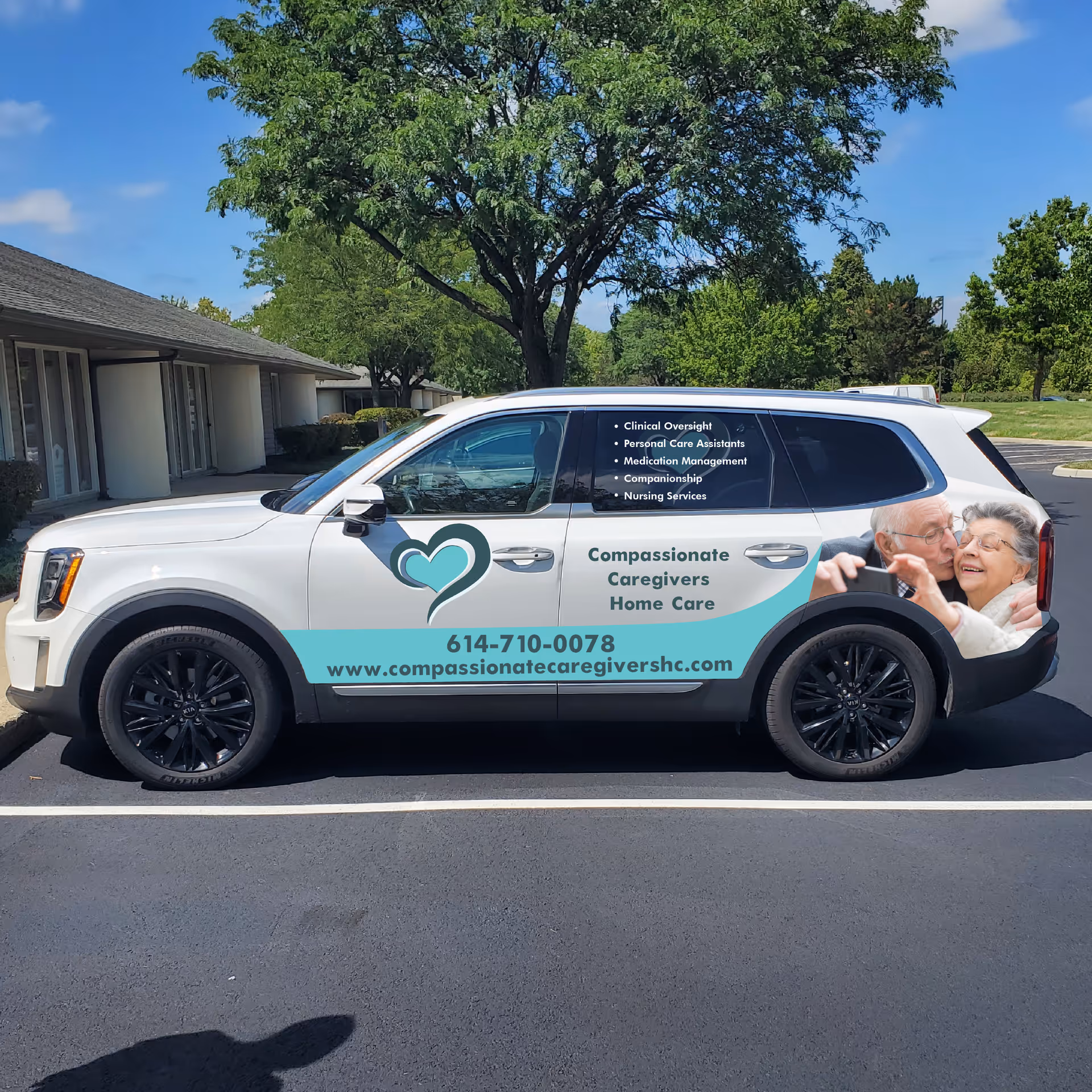 White Compassionate Caregivers van parked in a lot beside a building and trees.