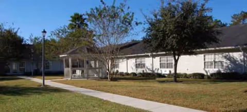 A single-story senior living facility with walkway, lawn, and trees in front.