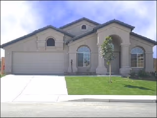Single-story beige residential building with arched windows, a two-car garage, and a manicured front lawn.