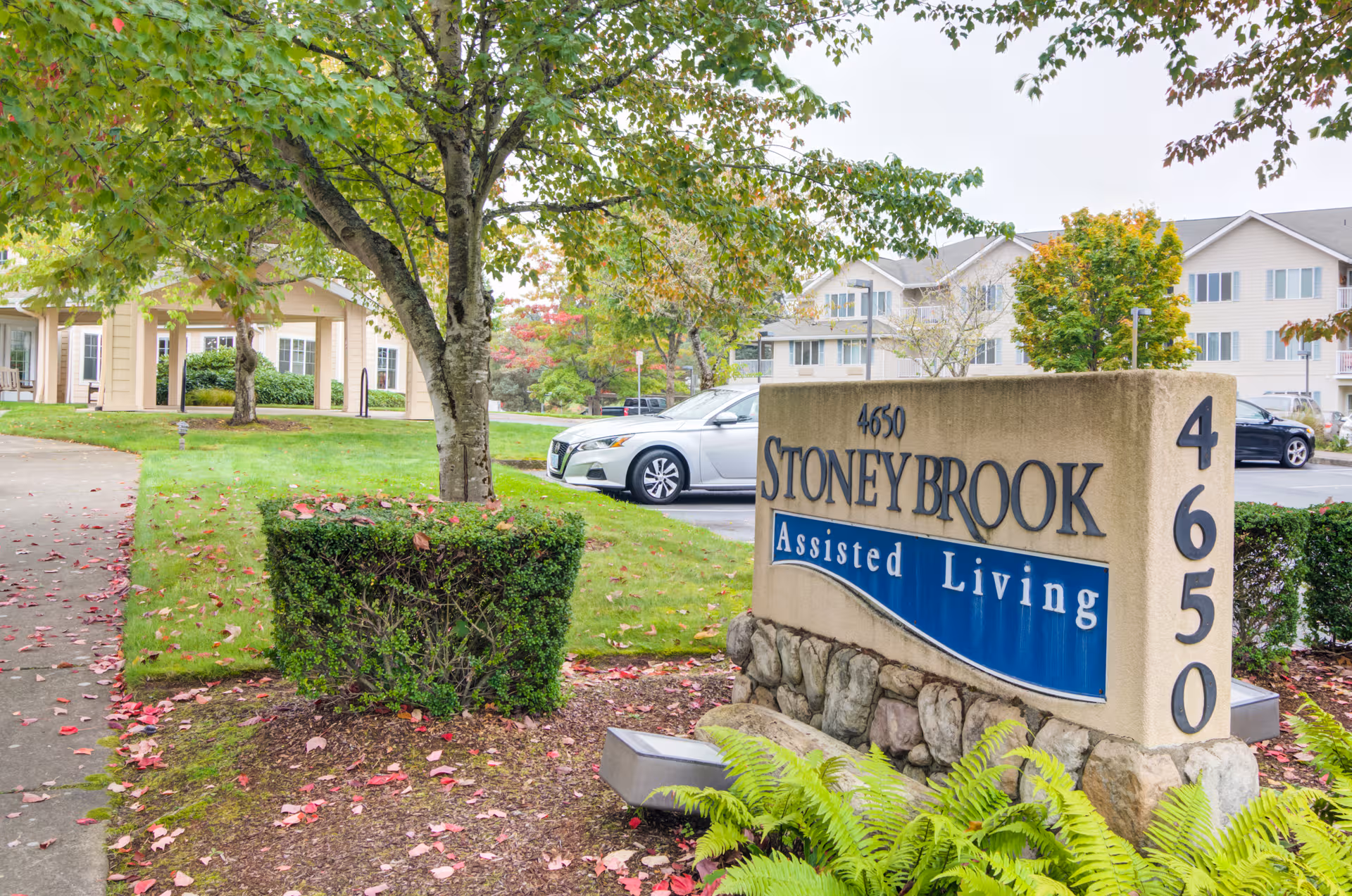 Front exterior of Stoney Brook Assisted Living with a large stone sign and landscaping.